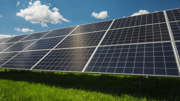 Zonnepanelen tegen de blauwe lucht met wolken en groen gras eronder — Stockfoto