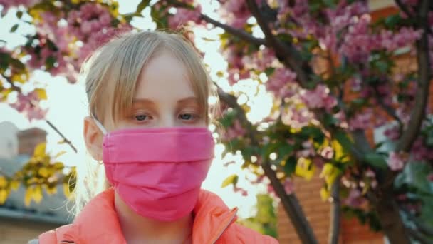 Meisje in roze beschermend masker tegen kersenbloesems — Stockvideo