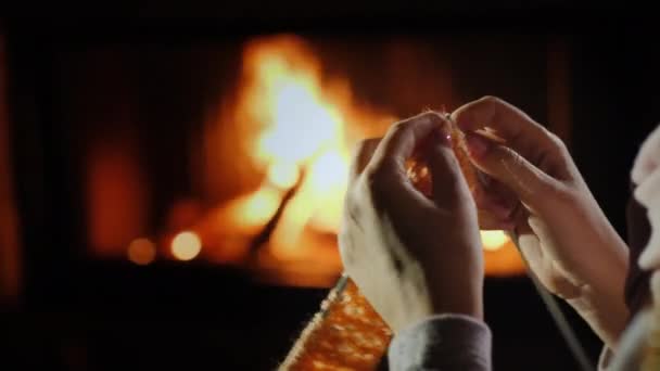 Tangan wanita dengan jarum rajut - merajut pakaian hangat yang duduk di dekat perapian — Stok Video