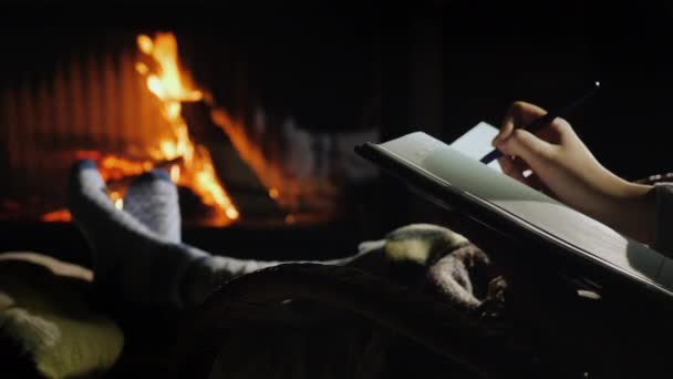 暖炉のそばに座ってノートに書く。新しい年の計画は、空白のシートの概念から始まります — ストック動画