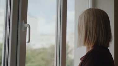 Yan görüş: Bir kadın yüksek katlı bir binanın dairesinde cam siliyor.