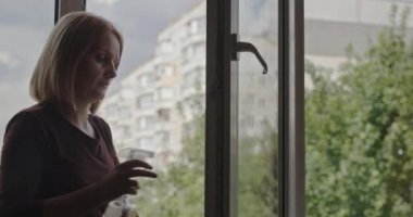 Bir kadın, yüksek bir binanın dairesinde cam siliyor..