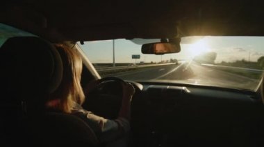 Kadın sürücü gün batımında otoyolda araba sürüyor.