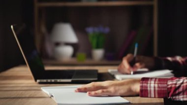 İşadamı dizüstü bilgisayarın yanında çalışıyor, defterine yazıyor.