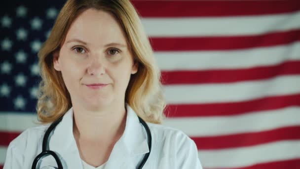 Retrato de uma jovem médica contra o pano de fundo da bandeira americana — Vídeo de Stock