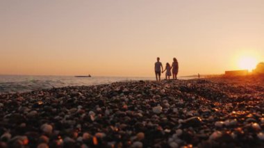 Gün batımında deniz kenarında bir çocukla birlikte bir tatil köyünde dinlenen bir aile.