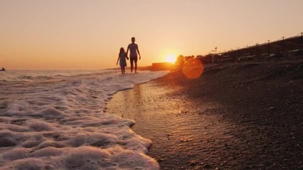 Erkek ve kız kardeş gün batımında deniz kıyısında yürüyorlar. — Stok video