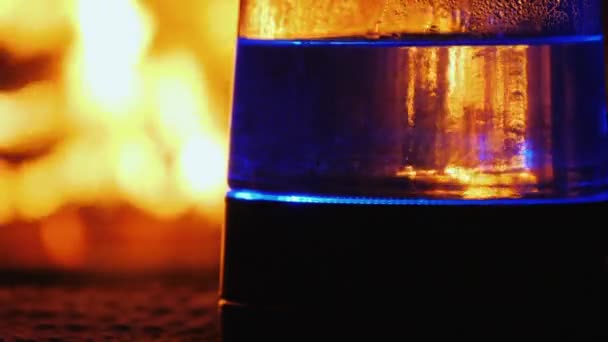Вода в прозрачном чайнике кипит на фоне огня в камине — стоковое видео