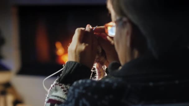 Mujer mayor teje una bufanda caliente junto a la chimenea — Vídeos de Stock