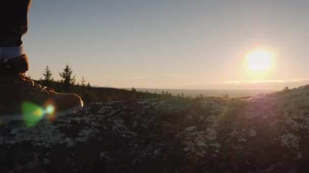 Мандрівники ноги на вершині піку, через них сяє висхідне сонце і красивий пейзаж на відстані — стокове відео