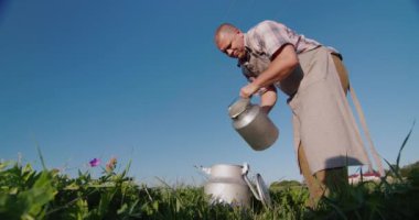 Çiftçi yeşil bir çayırın arka planına süt döker. Düşük açılı çekim
