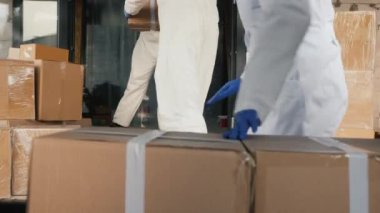 Nakliyecilerden oluşan bir ekip kutuları arabaya yüklüyor. Hepsi koruyucu antiviral kıyafetlerle.