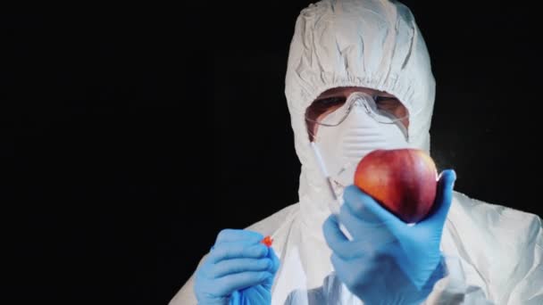 En mann i beskyttende klær og hansker tar en bit av et stort eple. Kontroll av anlegg – stockvideo