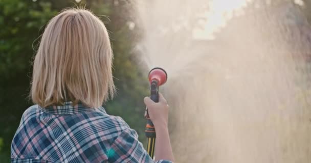 Back view: Gardener pours plants from garden hose — стокове відео