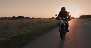 Motosikletli bir adam, otoyolda batan güneşin ışınlarında gidiyor. Yavaş çekim.