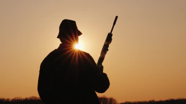 Silhueta de um caçador masculino com uma arma, olhando para a frente na frente dele, o sol está brilhando por causa de sua cabeça — Vídeo de Stock