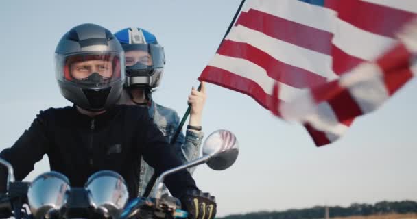 Motociclista com namorada senta-se na motocicleta, mulher detém bandeira dos EUA — Vídeo de Stock