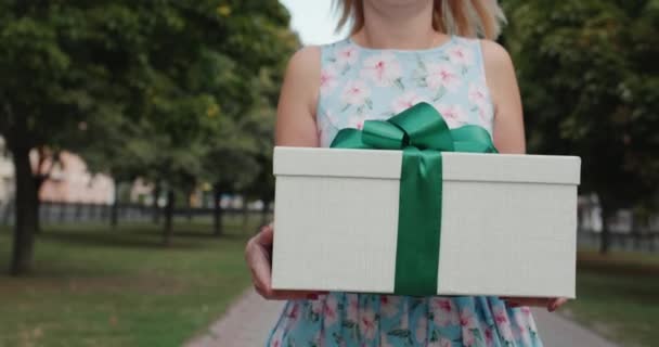 Жінка в літній сукні несе подарунок у красивій коробці, йдучи по вулиці міста — стокове відео