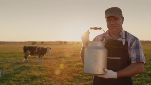 Портрет молочника с молочной банкой на фоне луга, где корова пасется — стоковое видео