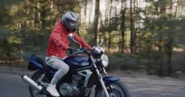 Genç motosikletçi orman boyunca hızla yol boyunca gider.