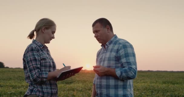 Zwei Bauern arbeiten auf einem Feld, studieren Pflanzen, machen Aufzeichnungen in einem Tagebuch — Stockvideo