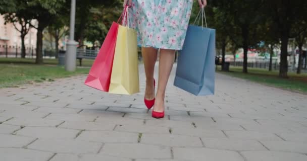 Kobieta w czerwonych butach na wysokim obcasie nosi wielobarwne torby na zakupy ze sklepu z modą. — Wideo stockowe