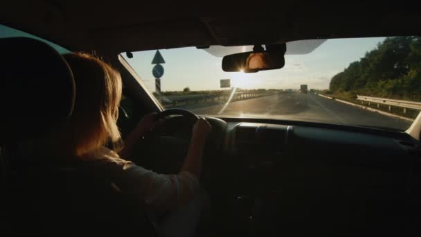 Mulher motorista ao volante de um carro dirige na estrada ao pôr do sol — Vídeo de Stock