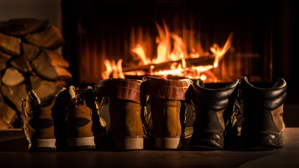 Alguns pares de sapatos de inverno estão secando perto da lareira onde o fogo está aceso — Fotografia de Stock