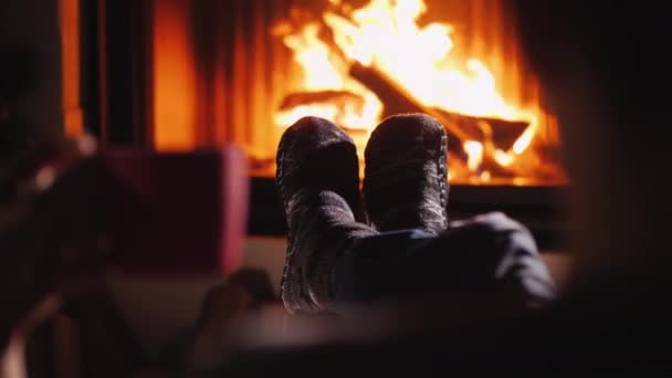 男が暖炉のそばで休んでいて、手にお茶を持っている。フレーム内の靴下のみが表示されます。 — ストック動画