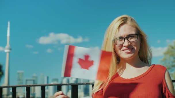 Glückliche Frau mit kanadischer Flagge vor dem Hintergrund von Toronto. Lächelnd in die Kamera schauen — Stockvideo