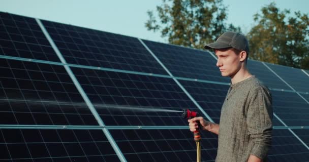 Jeune homme lave hors des panneaux solaires de tuyau — Video