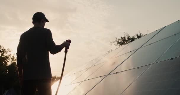 Σιλουέτα ενός άνδρα που πλένει ένα πάνελ ηλιακής ενέργειας — Αρχείο Βίντεο
