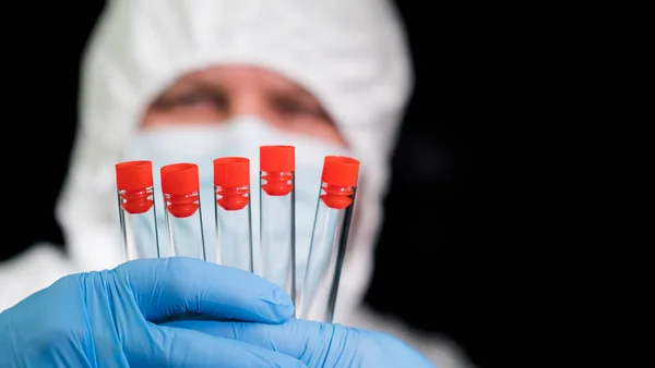 Cientista em terno de proteção detém tubos de ensaio com amostras — Fotografia de Stock