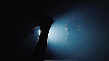 Karanlıkta dua eden kadın ve erkeklerin siluetleri, sahne ışıkları arkadan parlıyor.