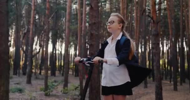 A girl in school uniform rides an electric scooter through the park — Stock Video