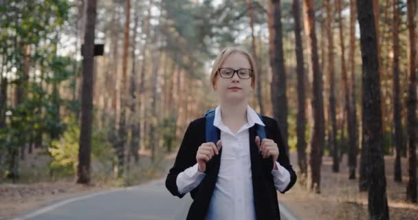 Uma criança com um pacote nas costas caminha sozinha através de um parque com árvores altas. — Vídeo de Stock