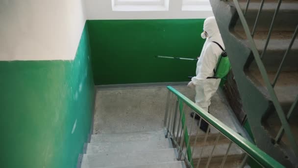 Travailleur en vêtements de protection pulvérise les escaliers d'un immeuble avec antiseptique — Video