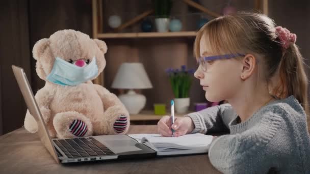 Anak itu belajar di rumah selama karantina, duduk di dekat laptop, di samping mainan dengan topeng pelindung — Stok Video