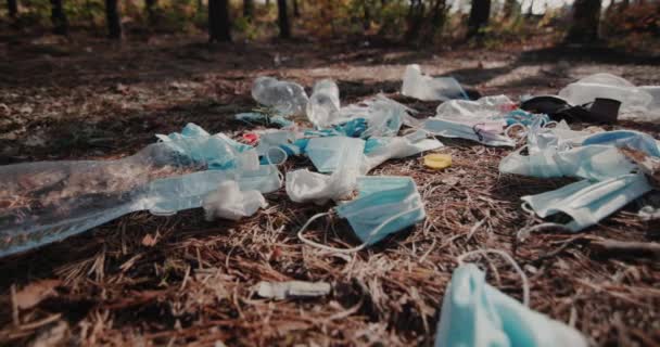Lente larga tiro: detritos de máscaras médicas e plástico encontra-se no chão na floresta — Vídeo de Stock