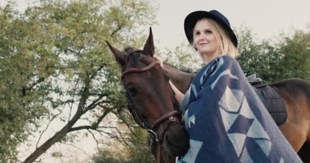 Retrato de uma mulher elegante em um chapéu e poncho perto de um cavalo — Vídeo de Stock