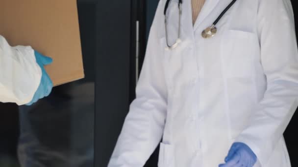 Доставляючи в лікарню коробку ліків, працівник клініки приймає ліки в двері — стокове відео