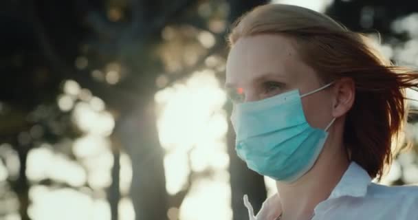女は医療マスクを外し自由にため息をつく。森の中に立つと、風が彼女の顔に吹く — ストック動画