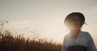 Elbiseli ve şapkalı bir kadın çiftçi olgun mısır tarlalarında yürüyor..