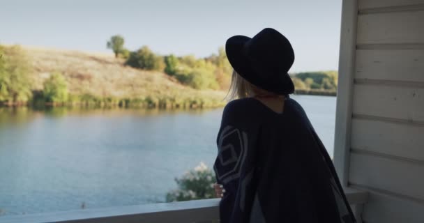 Eine Frau bewundert den Blick auf den malerischen See von der Veranda ihres Hauses — Stockvideo