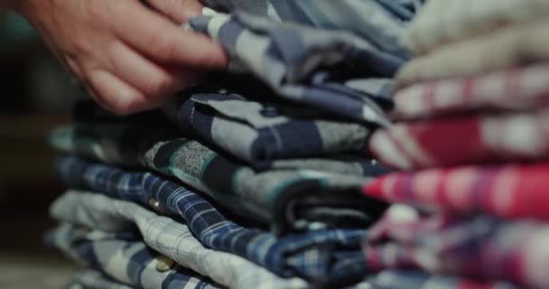 Вид сбоку: женские руки разбирают стопку футболок — стоковое видео
