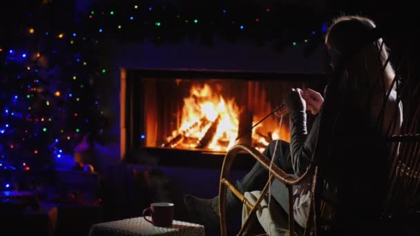 Rear view of a woman knitting while sitting by the fireplace — Stock Video