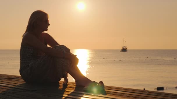 Romantisk kvinna med bagage tittar på fartyget långt ut i havet. Vid soluppgången — Stockvideo