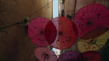 Dar bir Roma geçidinde asılı dekoratif şemsiyeler eski binalar arasında renkli gölgeler oluşturuyor ve yürüyen perspektife cazibe katıyor. Yüksek kalite 4k görüntü