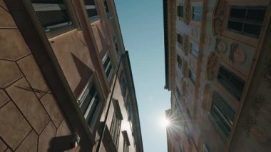 Yüksek binaları olan dar Roma caddesi ve çatılar arasında parlayan güneş. Yüksek kalite 4k görüntü