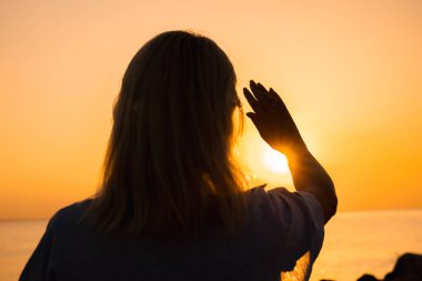 Denizin üzerinde gün doğumuna doğru elini kaldıran bir kadının silueti umudu, enerjiyi ve sağlıklı yeni bir günün başlangıcını simgeliyor. Yüksek kalite fotoğraf